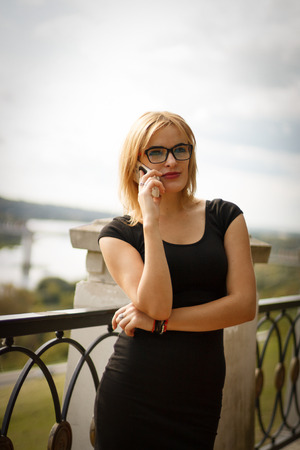 blonde woman at black dress and glases talking on a mobile phone outdoorsの写真素材