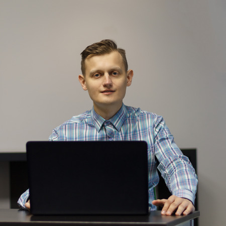 a young man in a blue shirt with a laptop at the table