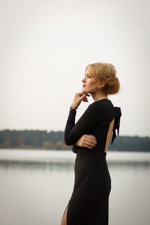 beautiful blonde girl in a black dress on the embankmentの写真素材