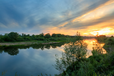 Scenic view of beautiful sunset above the river at summer with cloudy sky background and grass  at foreground. Landscape.の写真素材
