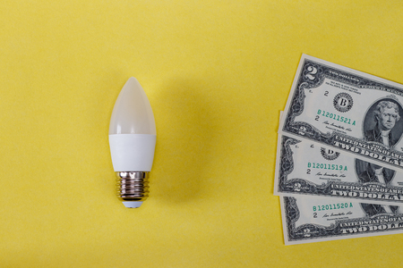 LED lamp on yellow background and dollar bills. The concept of saving money on electricity.