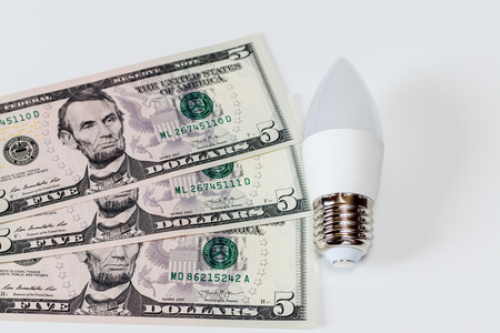 LED lamp on white table and dollar bills. The concept of saving money on electricity.の写真素材