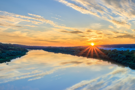 Sunset or sunrise on the river embankment at summer evening with clouds and trees. Landscape.の写真素材