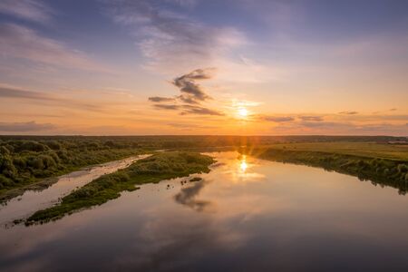 Aerial view to sunset on the river at summer evening with clouds and trees. Water reflection of a...