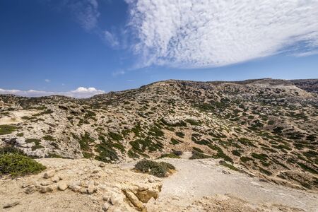 The coast and mountains of Matala on a clear summer sunny day with cliffs in the foreground and a cloudy sky in the background. Crete, Greece.の写真素材