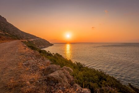 Sunrise on the island of Crete near Spinalonga with sea coast, rocks and dirt road on a summer morning.の写真素材