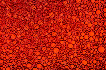 Top view on colorful drops of oil on the water. Circles and ovals. Abstract red background for...