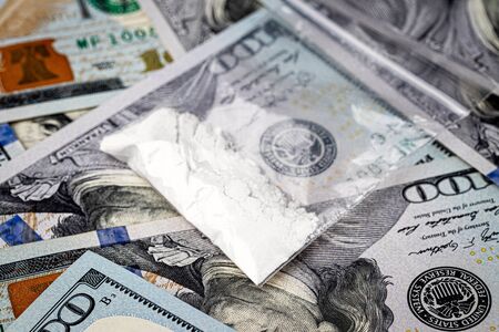 A bag with white narcotic powder like heroin or cocaine on the background of one hundred dollar bills. The concept of the use and sale of drugs.の写真素材