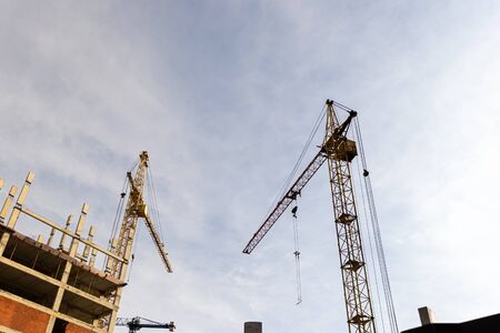 Boom cranes on a background of cloudy cloudy sky and building.