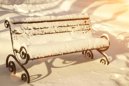 The bench is covered with snow and ice on a sunny winter day in the park.の写真素材