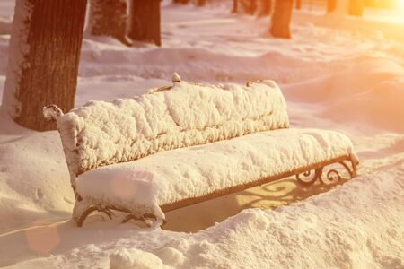 The bench is covered with snow and ice on a sunny winter day in the park.の写真素材