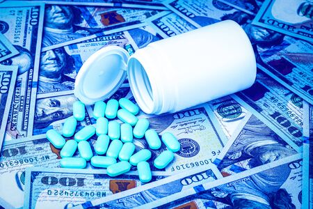 Green pills on the background of one hundred dollar bills. The concept of the expensive cost of healthcare or financing medicine. White medicine bottle with copy space for text.の写真素材