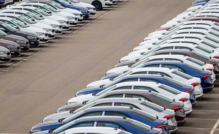 Rows of a new cars parked in a distribution center on a car factory on a cloudy day. Top view to the...