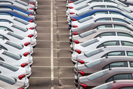 Rows of a new cars parked in a distribution center on a cloudy day in the spring, a car factory. Top...
