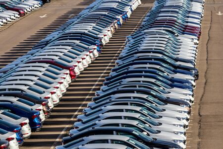 Rows of a new cars parked in a distribution center on a car factory on a sunny day. Top view to the...