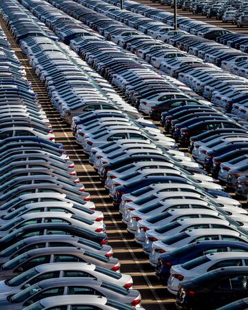 Rows of a new cars parked in a distribution center on a car factory on a sunny day. Top view to the...