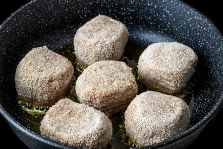 Raw frozen breaded chicken cutlets, heated in a ceramic black skillet with vegetable oil. The...