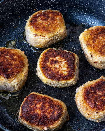 Breaded chicken cutlets, heated in a ceramic black skillet with vegetable oil. The process of frying steaks. Traditional cuisine.の写真素材