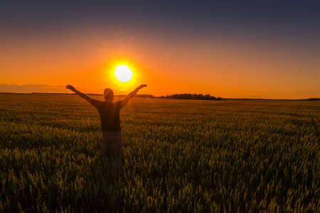 A man with his hands raised up against the backdrop of a sunset or dawn in a rye field. The concept...