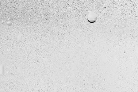 Rain drops on window glasses surface with gray sky background. Natural backdrop of raindrops. Abstract overlay for design. The concept of bad rainy weather.の写真素材