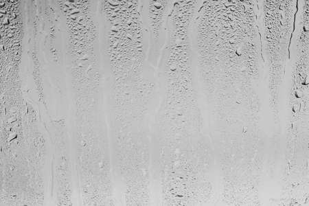 Rain drops on window glasses surface with gray sky background. Natural backdrop of raindrops. Abstract overlay for design. The concept of bad rainy weather.の写真素材