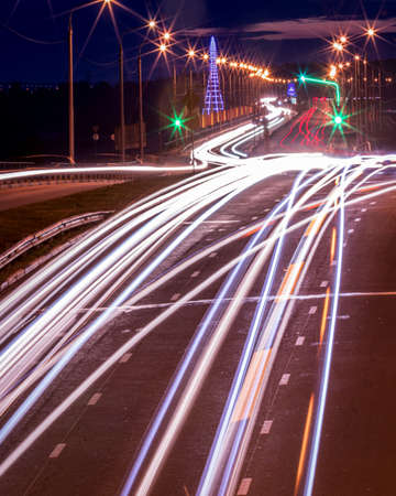 Traces of headlights from cars moving at night on the bridge, illuminated by lanterns. Abstract cityscape with highway at dusk.の写真素材