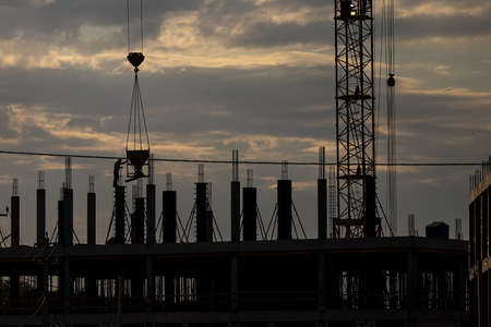 Silhouette of a team of construction workers in and a crane constructing a building on the...
