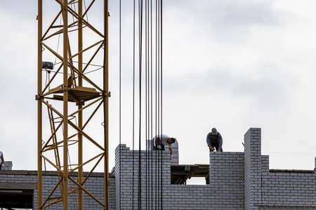 A team of construction workers in and a crane constructing a building on the background of the...