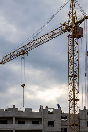 A team of construction workers in and a crane constructing a building on the background of the evening cloudy sky.の写真素材
