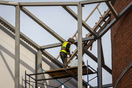 Russia, Kaluga - SEPTEMBER 16, 2020: Welder in a vest welding the metal frame of a building at a construction site on a sunny day.のeditorial素材