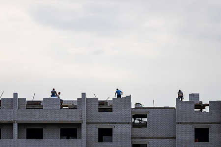 Russia, Kaluga - SEPTEMBER 16, 2020: Silhouette of a team of construction workers constructing a building in the cloudy day.のeditorial素材