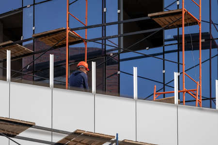 Russia, Kaluga - SEPTEMBER 16, 2020: Builder sitting on scaffolding at a construction site on a...