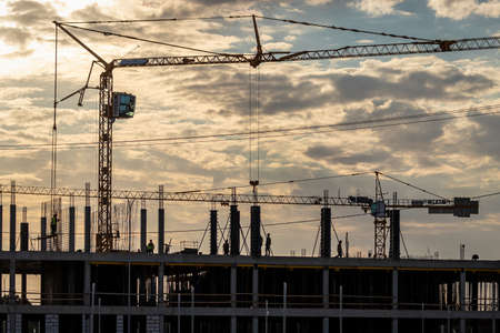 Russia, Kaluga - SEPTEMBER 16, 2020: A team of construction workers in and a crane constructing a building on the background of the evening sunset sky.のeditorial素材