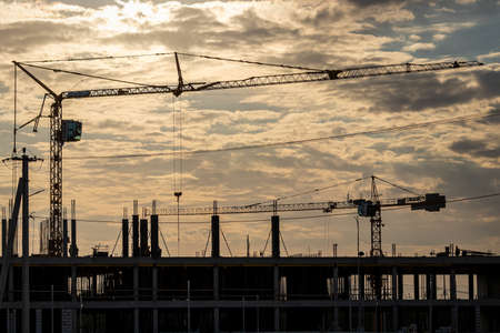 Russia, Kaluga - SEPTEMBER 16, 2020: A team of construction workers in and a crane constructing a building on the background of the evening sunset sky.のeditorial素材
