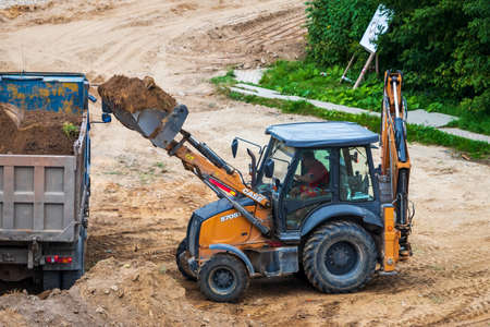 Russia, Kaluga - OCTOBER 27, 2020: Tractor carrying soil with a bucket to the back of a truck.のeditorial素材