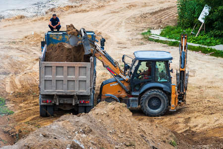 Russia, Kaluga - OCTOBER 27, 2020: Tractor carrying soil with a bucket to the back of a truck.のeditorial素材