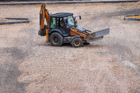 Russia, Kaluga - OCTOBER 27, 2020: Tractor with a bucket leveling gravel for road construction.