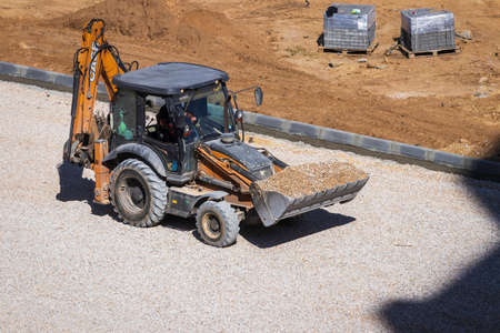 Russia, Kaluga - OCTOBER 27, 2020: Tractor with a bucket leveling gravel for road construction.