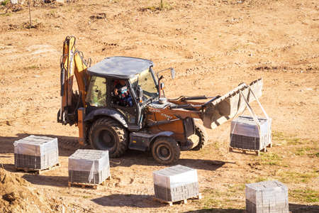 Russia, Kaluga - OCTOBER 27, 2020: A tractor carrying a bucket of new curbs for pavement...