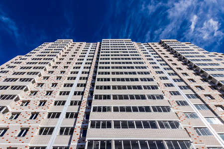 Fragment of a white brick residential building with balconies against a clear sky.