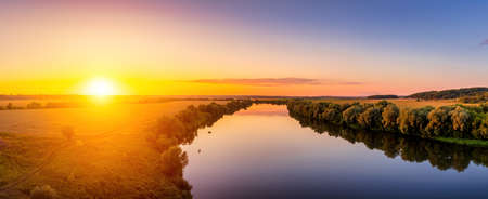 A sunset or sunrise scene over a lake or river with skies reflecting in the water on a summer evening or morning. Panorama.の写真素材