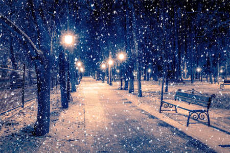 Snowfall in a winter park at night with christmas decorations, lights and pavement covered with snow. Falling snow.の写真素材