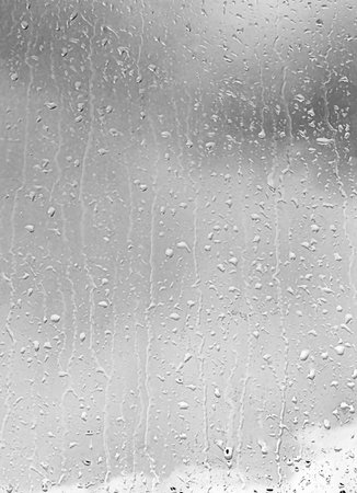 Rain drops on window glasses surface with gray sky background. Natural backdrop of raindrops. Abstract overlay for design. The concept of bad rainy weather.の写真素材