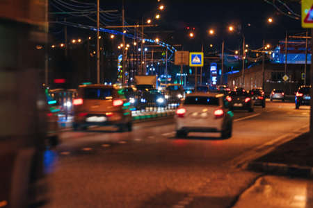Blurry lights of moving cars and lanterns reflecting on the wet asphalt in the night city. Bad...