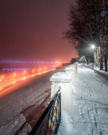 Winter park at night with glowing lanterns, view to road with car motion, pavement and trees in foggy weather.の写真素材