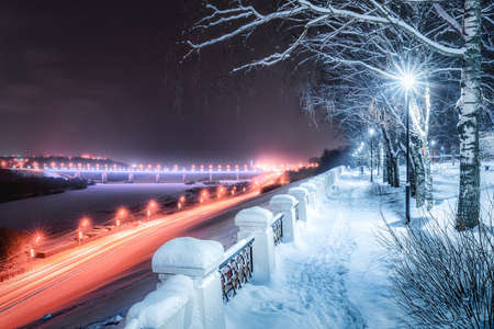 Winter park at night with christmas decorations, glowing lanterns, pavement covered with snow and trees.の写真素材