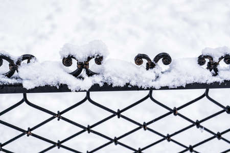 Black metal grate covered with snow in winter. Snowfall and winter weather concept.