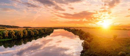 A sunset or sunrise scene over a lake or river with cloudy skies reflecting in the water on a summer evening or morning. landscape.の写真素材