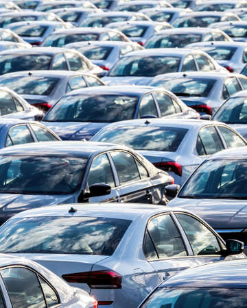 Rows of a new cars parked in a distribution center on a car factory parking.