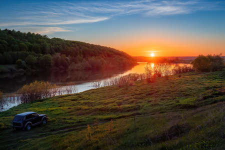 Sunset or dawn on the river in summer with a car on the bank.の写真素材